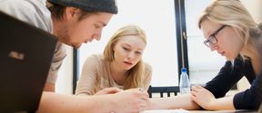 Three Aalto University students are doing group work by writing on paper together.