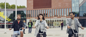 Thre students bicycling in front of the Väre building.