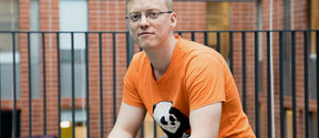 Jara Uitto sitting at Computer Science building, looking at the camera and wearing an orange t-shirt with a panda on it
