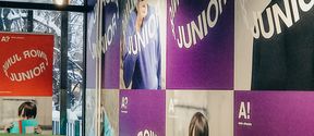Aalto-yliopisto Juniorin aulatila: värikäs julisteiden peittämä seinä ja vihreä kulmasohva