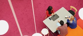 Ylhäältä otetussa kuvassa opiskelijat istuvat pöydän ääressä Oppimiskeskuksen värikkäissä tiloissa