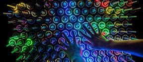 InteraktiiQuantum Garden on interaktiivinen elektroninen valotaideteos, jota koskettamalla teoksen värit muuttuvat. Tummasävyisessä kuvassa kaksi kättä kurkottaa eriväristen valoantureiden päälle.