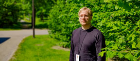 Heikki Nurmi outdoors on a sunny day in a black shirt in front of a background of leaves and trees.
