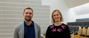 A man and woman in casual wear, dark tones, smiling at the camera inside the Aalto Hall.