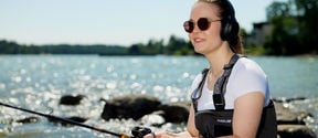 Woman fishing with headphones and listening an online course. Photo: Ari Toivonen