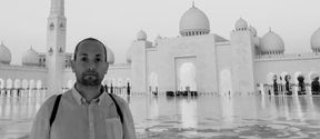 Mies seisoo mustavalkokuvassa suuren vaalean rakennuksen pihalla Abu Dhabissa
