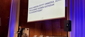 Kuvassa näkyy professori Teemu Malmi Aallon Töölön kampuksen juhlasalin lavalla pitämässä avauspuheenvuoroa Taloudenpuolustuskurssilla 2023. 