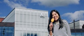 A student eating a yellow ice cream in fron of Aalto University campus.