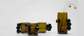 A collection of dark green-brownish glass mugs and a vase with blob like ornamental handles