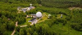 Metsähovi radio observatory photographed from a bird's eye view. A radio observatory in the middle of a green forest landscape.