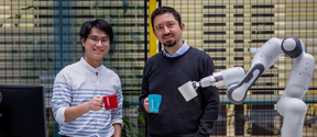Two of the awardees and their robotic arm all holding colorful mugs. Aalto Open Science Award, Honorary mention.