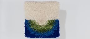 A square textile art piece in white, green and two different shades of blue