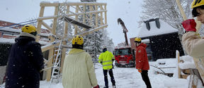 Students wearing helmets outside in the snow, with a large part of the timber structure next to a crane.