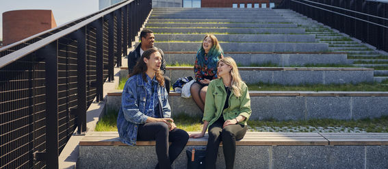 Four people sitting on stairs outside on campus in sunlight