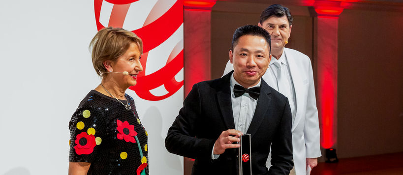 Hymyilevä tummapukuinen Chao Yang esittelee juuri saamaansa palkintoa Red Dot Awards -palkintoseremoniassa