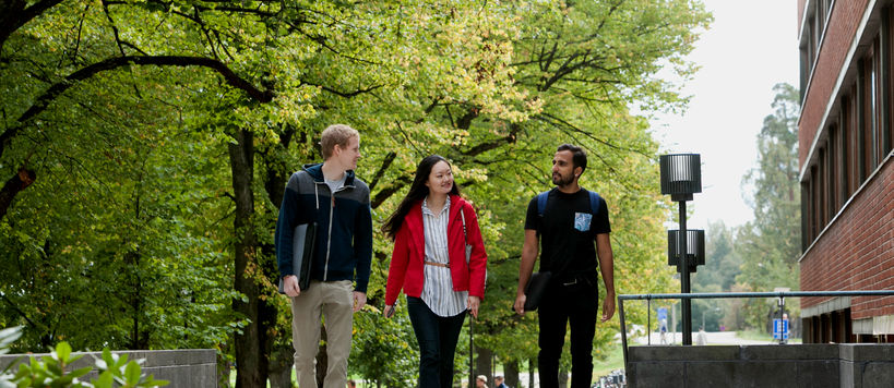 Three students in autumn walking on Aalto University campus, near Harald Herling Learning Centre.