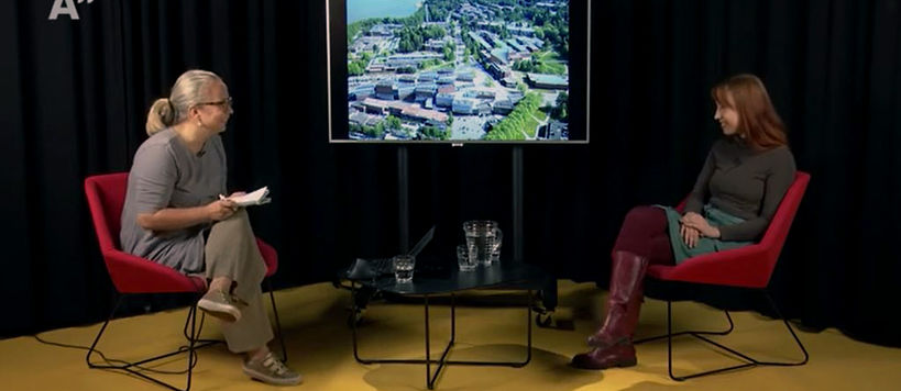 kaksi naista istuu punaisilla tuoleilla studiossa keskustelemassa, taustalla musta verho ja keltainen lattia 