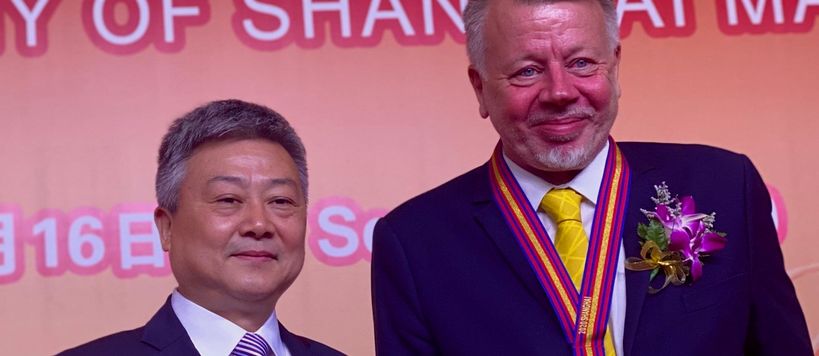 kuvassa kaksi miestä, joista toinen esittelee mitali kaulassa saamaansa kunniakirjaa punaisissa kansissa