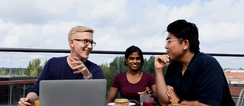 Students discussing around a laptop on an outside terrace during a summer course at Aalto University Summer School.