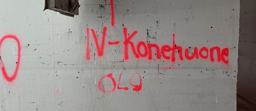Image depicts a white wall with the words IV Konehuone OLO sprayed on it in red, referring that the engine room for AC is that way.