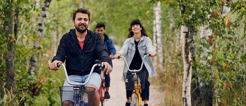 Three smiling students cycling in Otaniemi in the summer.