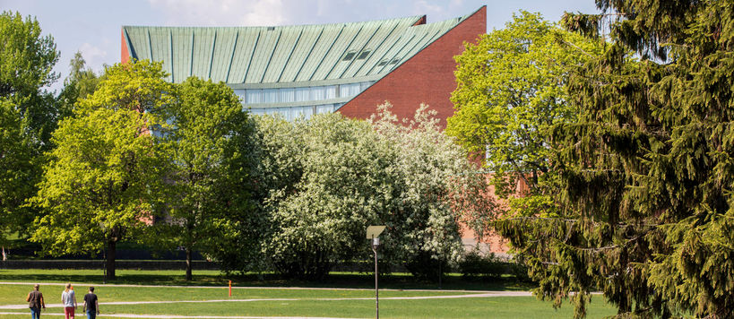 Aalto University campus building behind fresh green trees. Photo: Aalto University / Mikko Raskinen