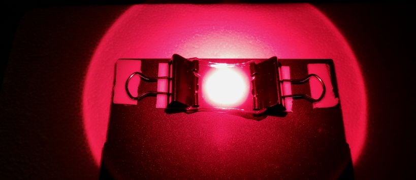 A gel being lit by a bright red light and stretched between two clips. 
