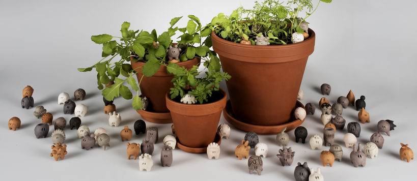 three plants in pots and heaps of little ceramic creatures around them