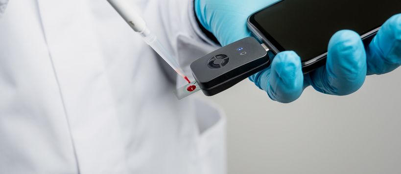 Valkoinen laboratoriotakki sekä analyysityökalu, jolla voidaan mitata veripisarasta särkylääkkeen pitoisuus.