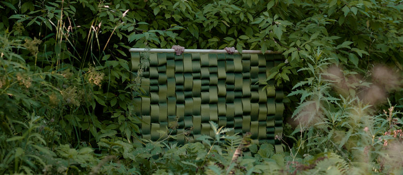 Two hands hold a green textiles surface surrounded by rich green nature all around  