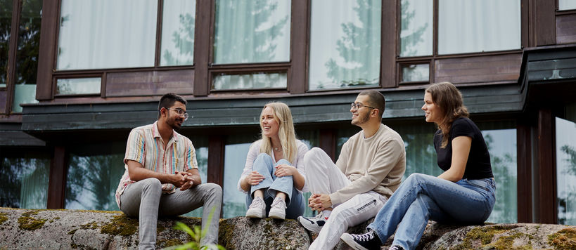 Four Aalto University students sitting outside on rocks and talking