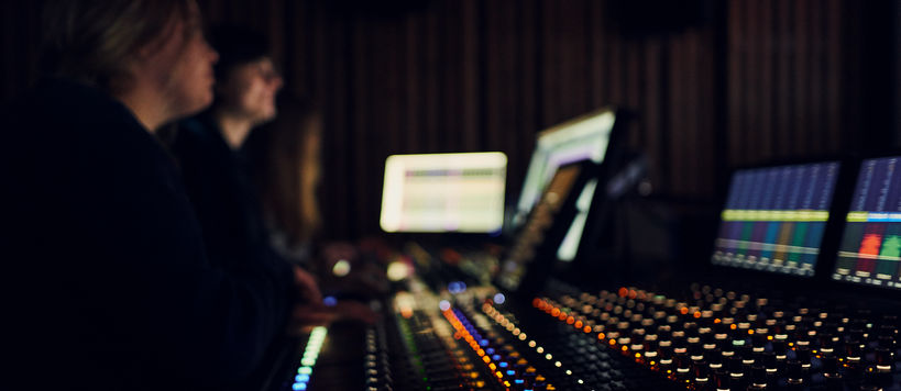 Two people seated next to an audio mixer