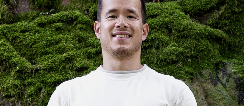 Hymyilevä mies katsoo kameraan taustanaan sammaleen peittämä kivi