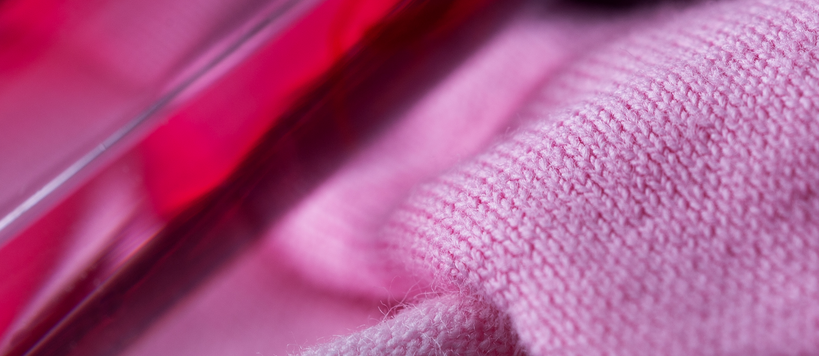 A close-up image of pink woven fabrics and a red bottle of fabric dye.