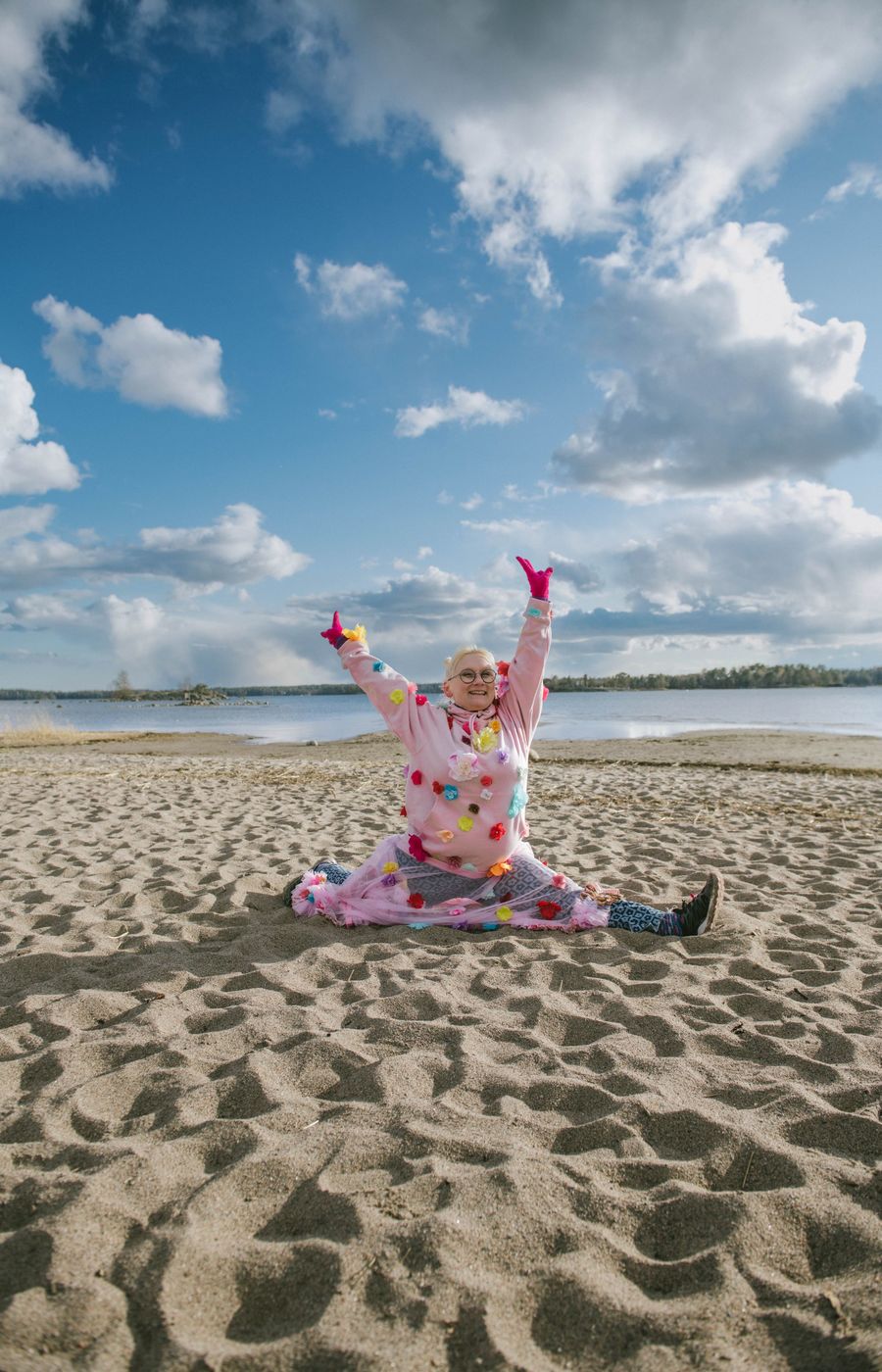 A blond woman in a pink suit making gymnastic movements on the beach