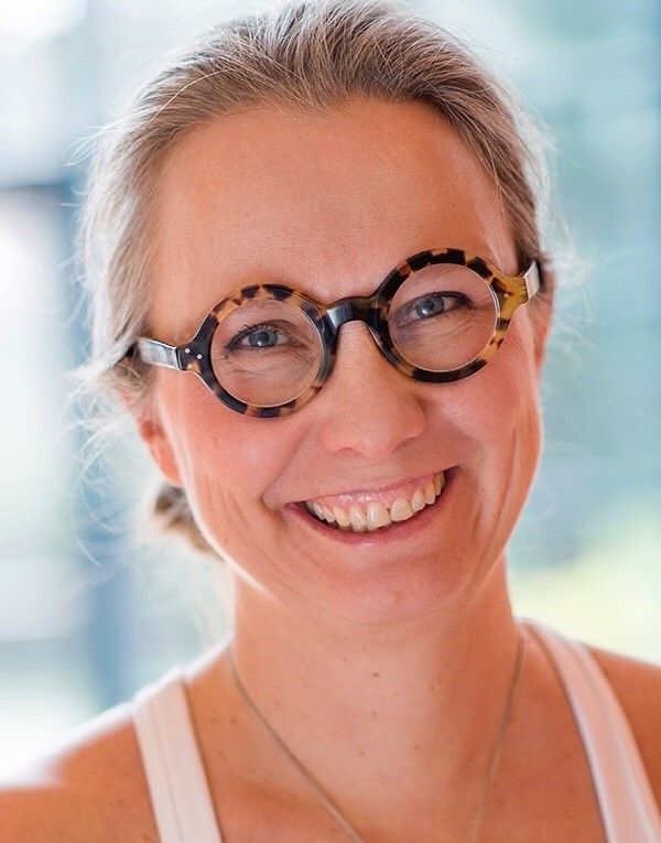 Professor Laura Arpiainen in glasses and a white top, smiling happily into the camera.