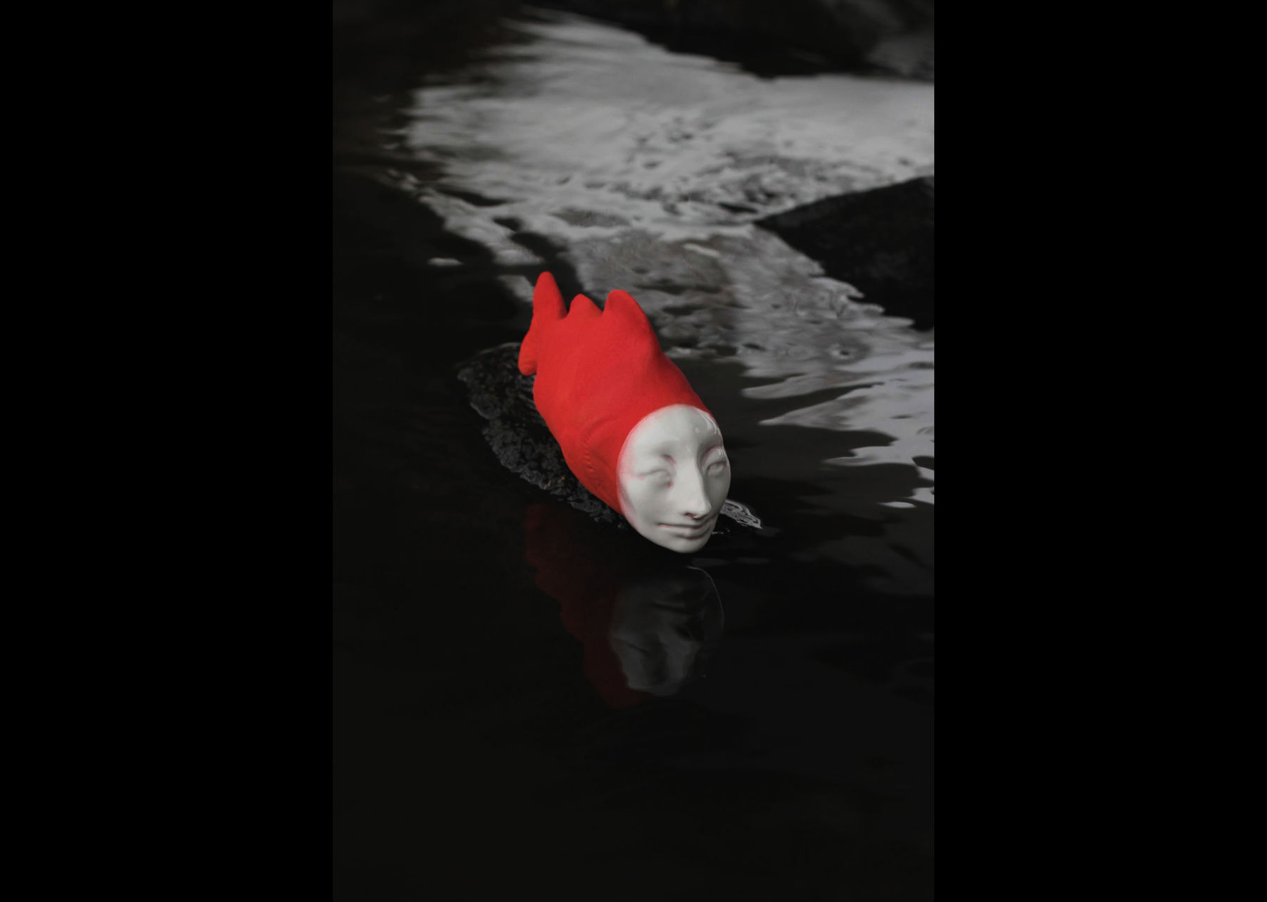 a ceramic fish with human-like face and red body with black background