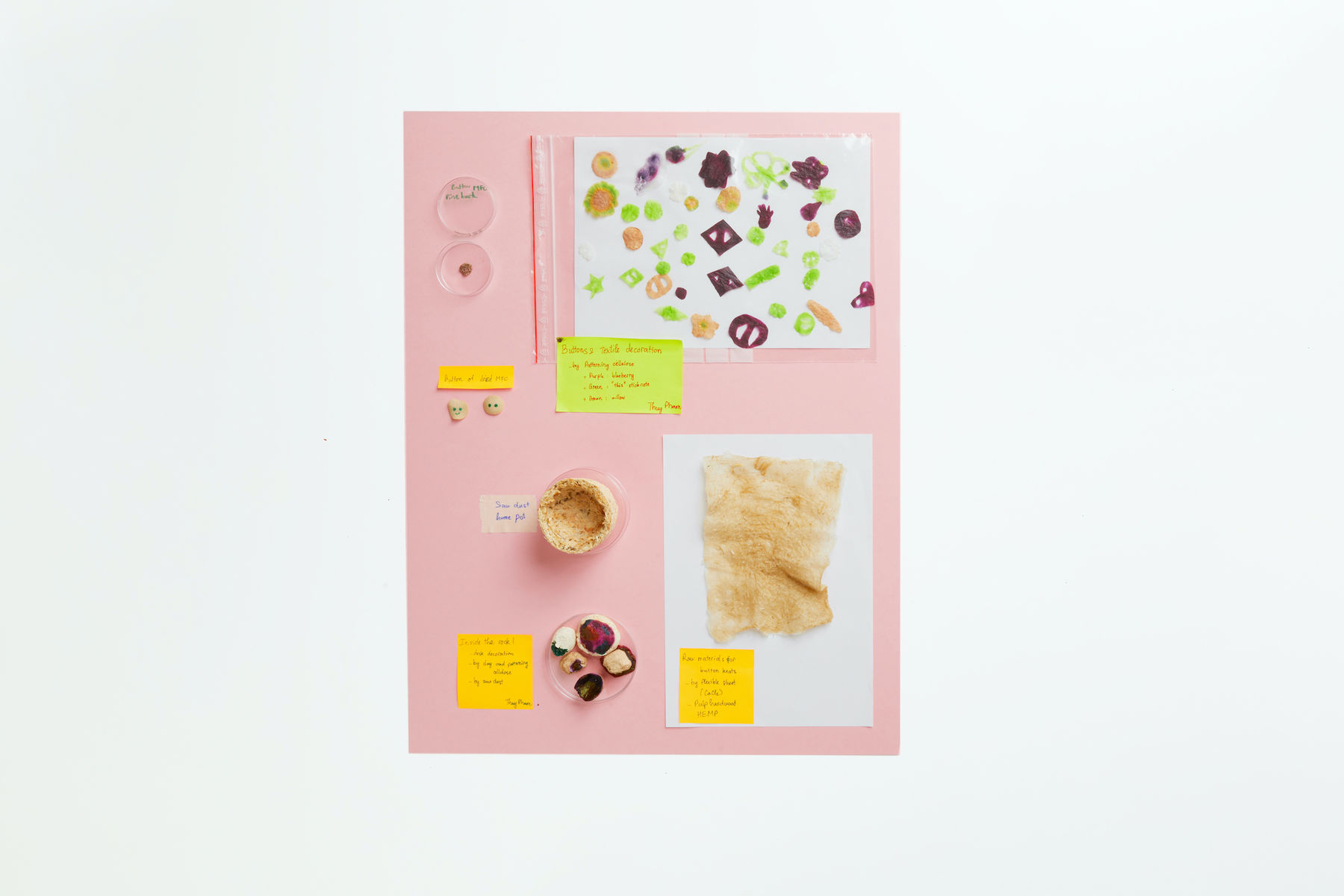 Portfolio photo of items produced while experimenting in the laboratories during the Aalto University Summer School course Nordic Biomaterials with CHEMARTS. The times are displayed on a light pink background and photographed from above. The items are different types of paper and items produced out of biomaterials such as beige buttons of dried MFC, a pot made of saw dust.