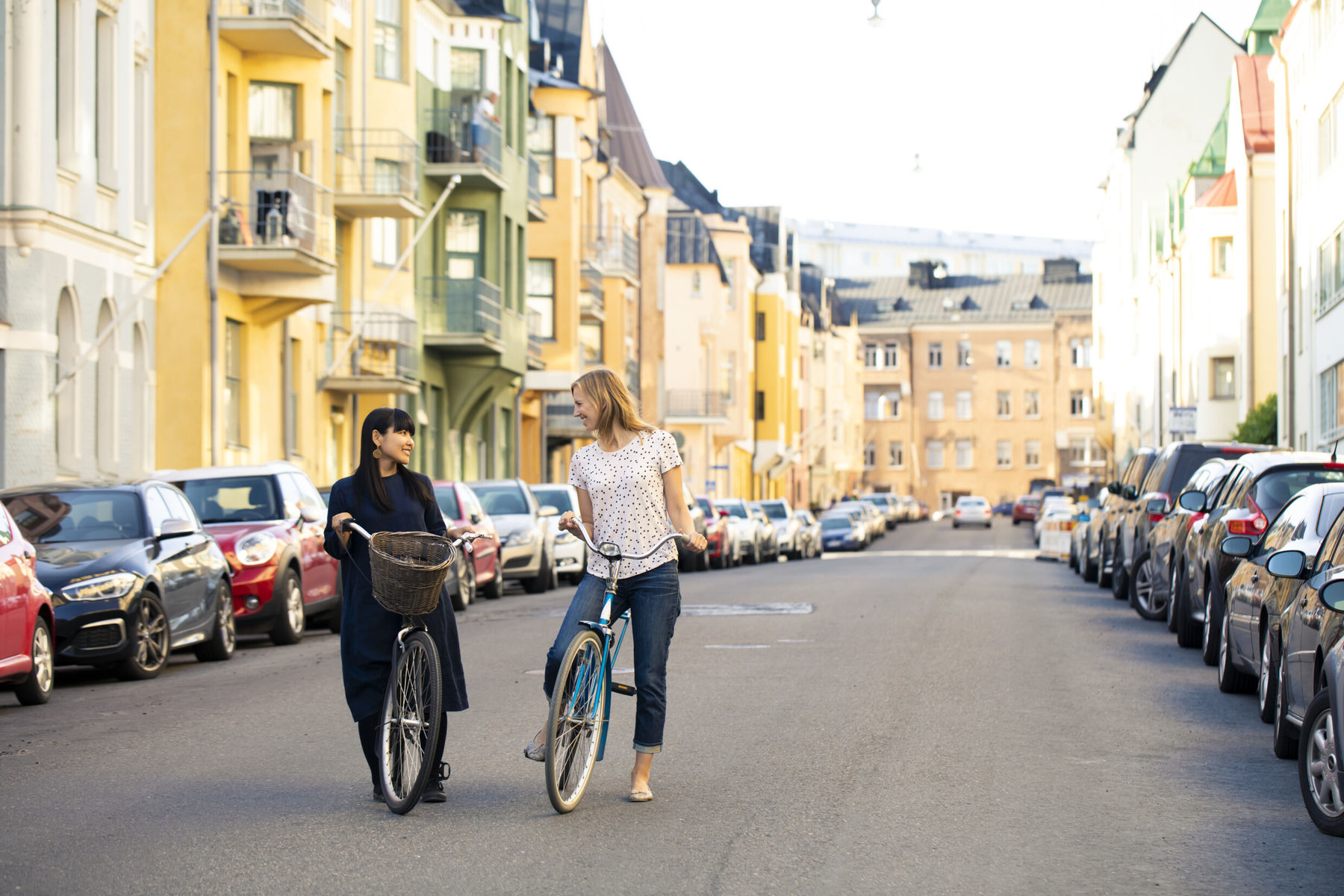 Two women on bikes surrounded by colourful house fasades on Huvilankatu in Ullanlinna neighbourhood, Helsinki.