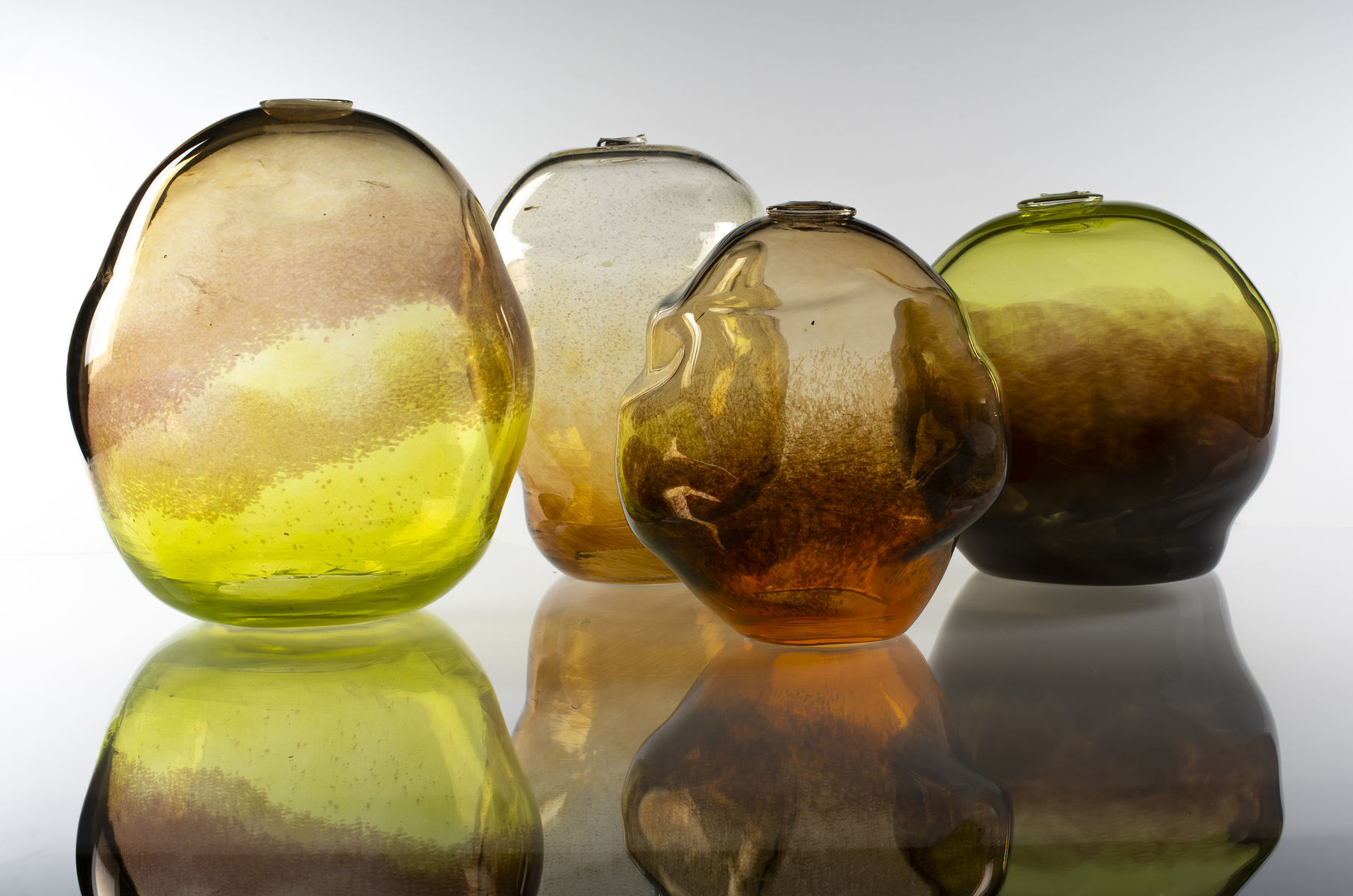 four nature-coloured glass objects with reflections underneath them