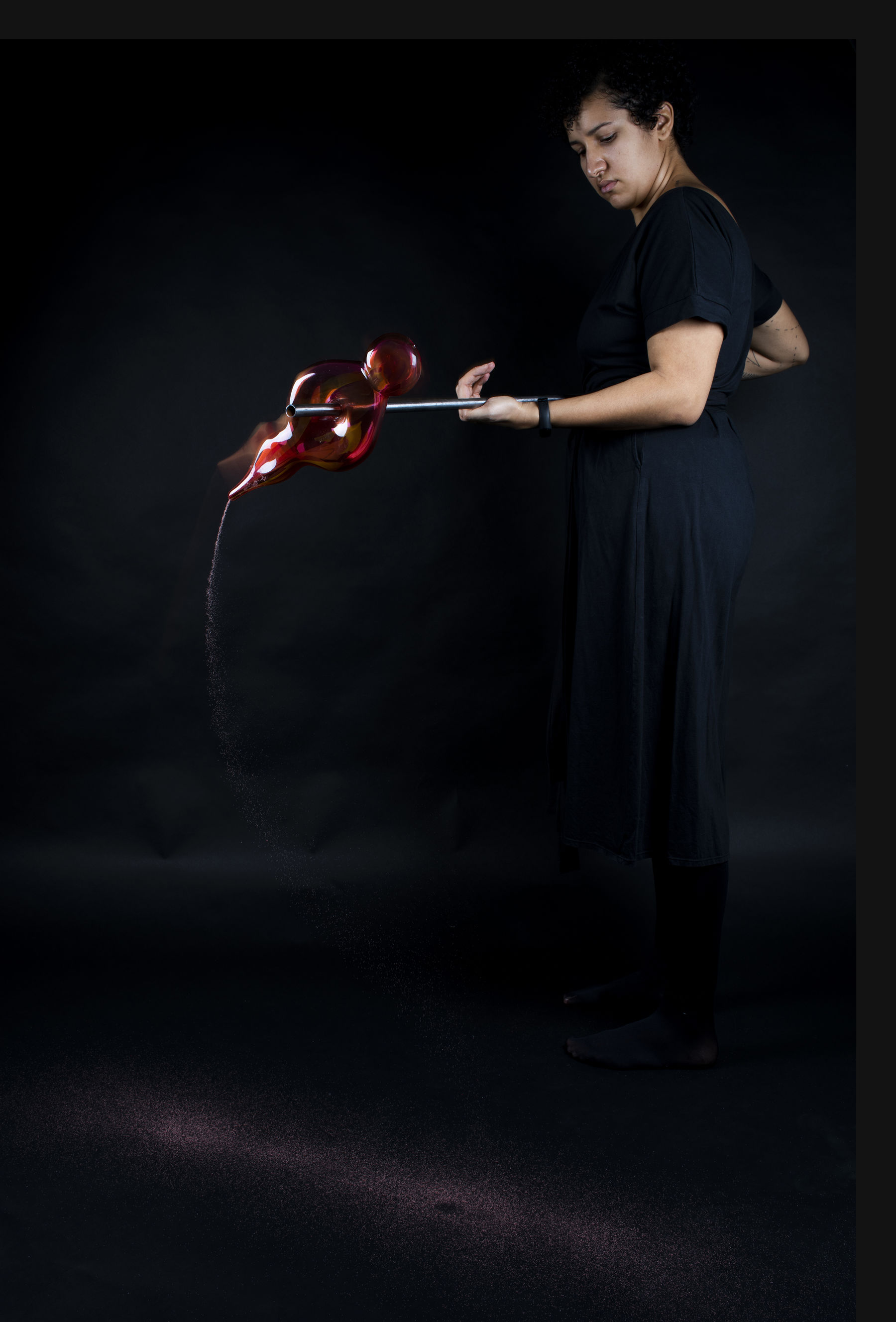 a person holding a glass blowing tool with a glass scultupre on it with dark background
