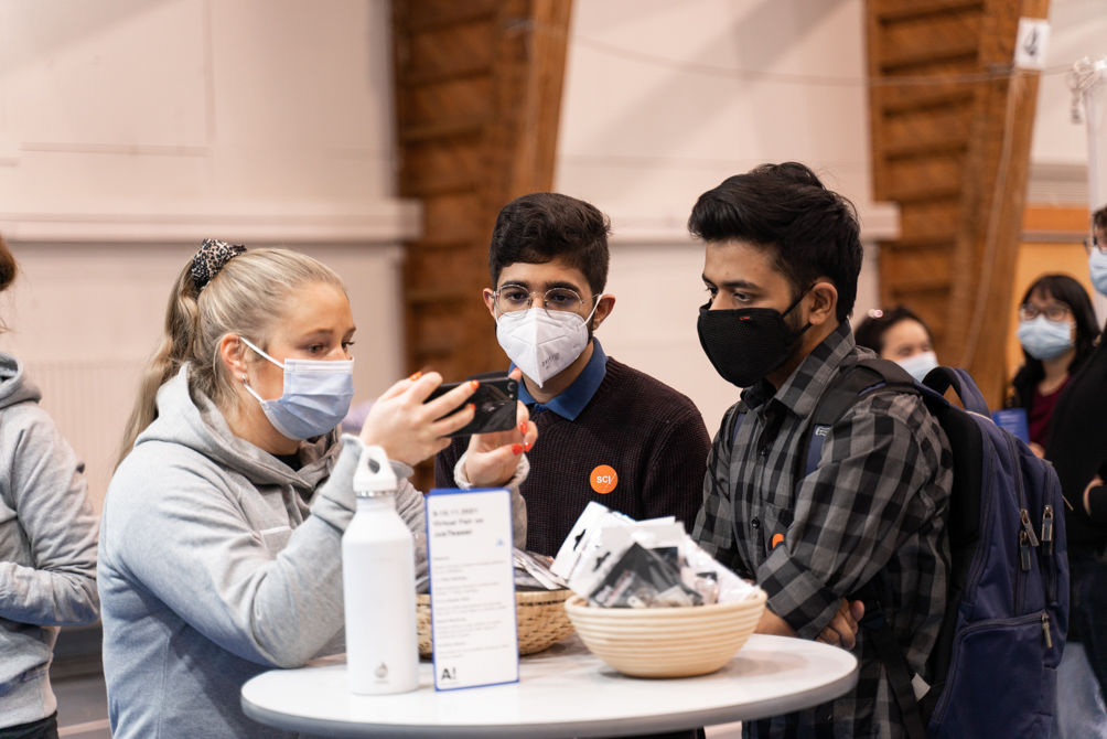 Students with a mask on huddled on a table checking out the fair map on a phone
