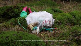 a person in a protective plastic suit lays on the ground in the woods exploring the bog and saying: 'It's so hard to slow down, if I moved 2cm a day maybe that would work better.