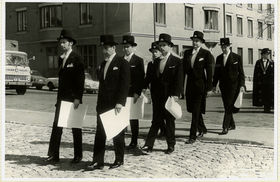 Mustavalkoisessa kuvassa tohtorit kävelevät rinnakkain todistukset kädessä.
