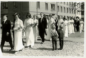 Mustavalkoisessa kuvassa kaksi pikkupoikaa katselee juhlavaatteisiin pukeutuneita promovendejä puolisoineen, jotka kävelevät kulkueessa