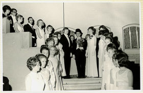 Mustavalkoisessa kuvasssa promoottori ja juhlapukuisia promovendejä puolisoineen seisoo rappusilla.