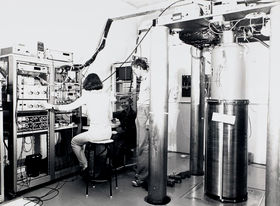 Research group. Pictured right is a large column with a warning sign for a high magnetic field area. Laboratory staff work on several measuring devices. 1970s-1980s. University of Technology. Photo: Aalto University Archives