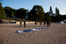 A group gathers outdoors on Hietaranta next to Hietsun Paviljonki. The sun is setting and one artwork from the project lays in the sand.