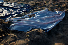 A blue and white satin fabric lays embedded in the sand. An artwork by Pia Euro and Tanja Koponen