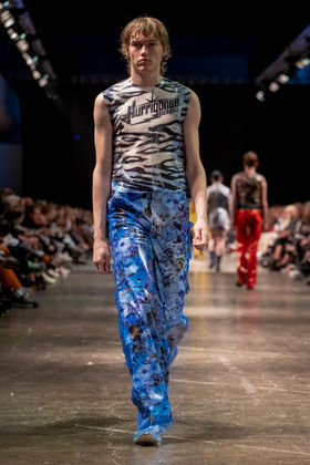 model on runway in shiny blue pants and grey shirt